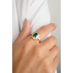 a woman's hand wearing a gold ring with an emerald stone in the middle