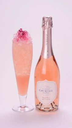 a bottle of champagne next to a glass filled with ice and pink sprinkles