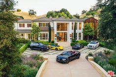 luxury cars are parked in front of a large white house with trees and bushes around it