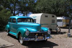 an old blue car is parked next to a trailer and camper in the background