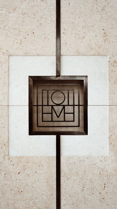 a square metal object on the side of a white tile wall with an embossed design