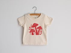 This super-soft unisex kids tee was designed with love and screen printed by hand in-house. Original woodland mushroom illustration is printed in crisp red ink on 100% organic cream cotton fabric. Made in the USA and hand-printed in our Ohio studio. Perfect for outdoorsy little ones, adventurous tots, nature lovers, and fairy gardeners! All artwork is original. Sizes available in: * 3-6 Months * 6-12 Months * 12-18 Months * 18-24 Months * 2T * 4T * 6T * Youth Small * Youth Medium * Youth Large N Playful Organic Cotton Graphic T-shirt, Playful Organic Cotton T-shirt With Graphic Print, Playful Organic Cotton Graphic Print T-shirt, Cute Organic Cotton T-shirt With Screen Print, Summer Cotton T-shirt With Mushroom Design, Cotton Summer T-shirt With Mushroom Design, Cotton Crew Neck T-shirt With Mushroom Print, Cotton T-shirt With Mushroom Print, Crew Neck, White Cotton T-shirt With Mushroom Design