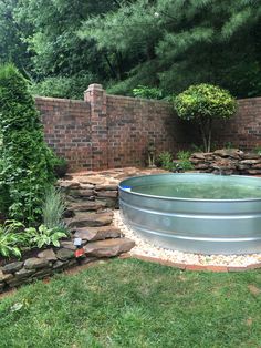 a large metal tub sitting in the middle of a lush green yard next to a brick wall