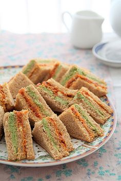 a plate full of sandwiches on a table with cups and saucers in the background