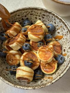 a bowl filled with blueberries and pancakes covered in syrup