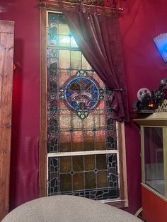 a stained glass window in the corner of a room with a gray chair and red walls