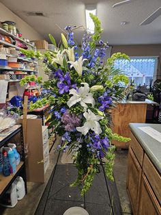 a bouquet of flowers sitting on top of a black stand in a room filled with shelves