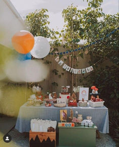 an outdoor birthday party with balloons, cake and desserts on a table in the backyard