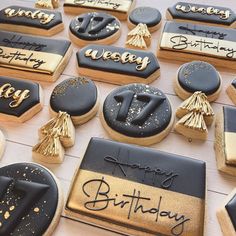 decorated cookies with black and gold icing are on a white tablecloth that says happy birthday