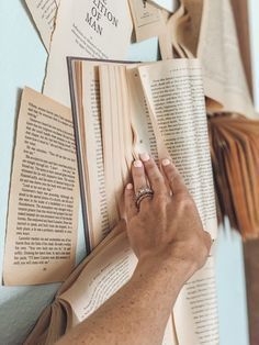 a person is holding an open book in front of several books on the wall with tassels hanging from it