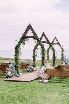 an outdoor ceremony setup with wooden benches and flowers on the grass, along with greenery