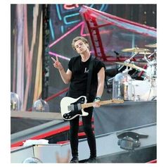 a man standing on top of a stage with a guitar in his hand and pointing to the side