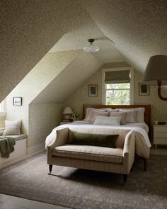 a bed sitting in the middle of a bedroom under a slanted ceiling next to a window