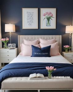 a bedroom with blue walls and pink flowers in vases on the bed, along with two framed pictures