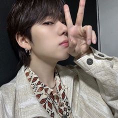 a young man making the peace sign with his hand while wearing a shirt and necklace