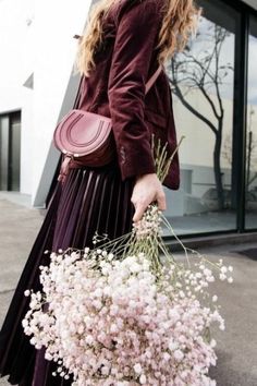 a woman walking down the street with flowers in her hand and a purse on her shoulder