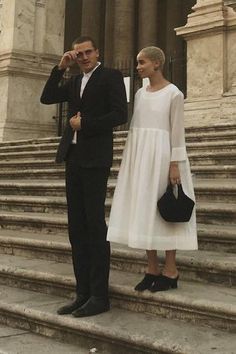 a man and woman standing on the steps in front of a building with stone stairs