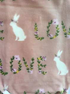 a baby's pink blanket with white rabbits and flowers on it that says love