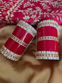 two red vases sitting on top of a bed covered in gold and pink fabric