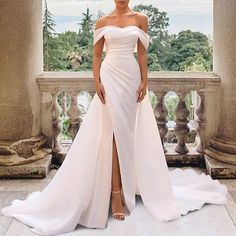 a woman standing in front of a window wearing a white dress with high slits