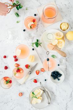 a table topped with plates and bowls filled with fruit next to glasses of water on top of a marble counter