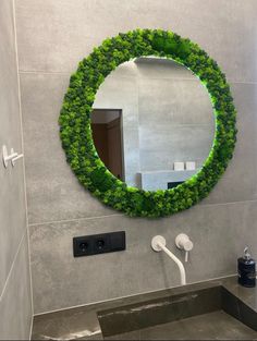 a bathroom with a circular mirror and green plants on the wall above it, next to a toilet paper dispenser