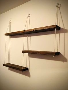 three wooden shelves hanging from ropes on the wall, one with two hooks attached to it