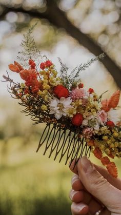 a person holding a comb with flowers on it in front of some grass and trees