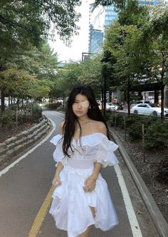 a woman in a white dress is walking down the street with her hand on her hip