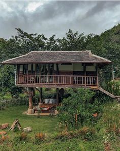 a wooden house sitting in the middle of a lush green field with lots of trees