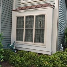 a house with two windows and bushes in the front yard, next to it is a clock tower