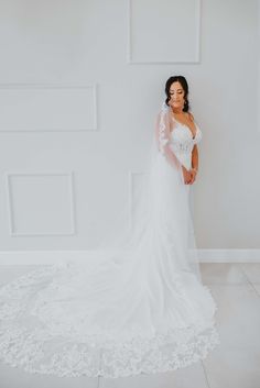 a woman standing in front of a white wall wearing a wedding dress with long sleeves