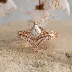 a close up of a diamond ring on a stone surface with flowers in the background