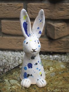 a white and blue bunny sitting on top of a rock next to a brick wall