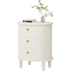 a white dresser with gold knobs and drawers on it's sides, next to a plant