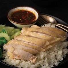 a black plate topped with rice and meat next to broccoli on a table