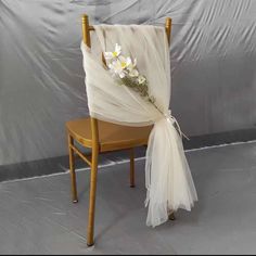 a chair with a white cloth draped over it and flowers on the back, sitting in front of a gray backdrop