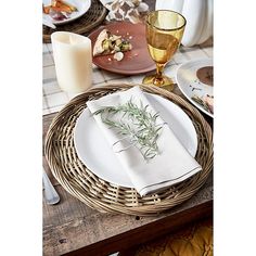 a table set with place settings, candles and napkins in wicker baskets on top of a wooden table