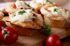 some food that is sitting on a wooden cutting board next to tomatoes and other vegetables