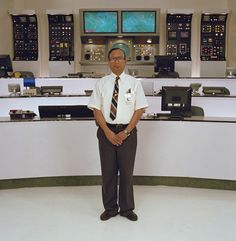 a man standing in front of two control rooms with multiple monitors on the wall behind him