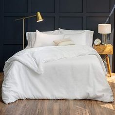 a white bed sitting next to a wooden table with a lamp on top of it