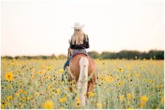 a woman riding on the back of a brown horse through a field of yellow flowers