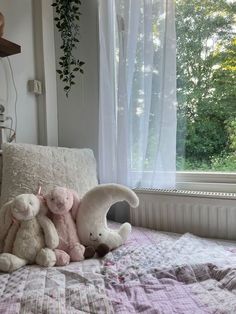 two stuffed animals sitting on top of a bed in front of a window with curtains