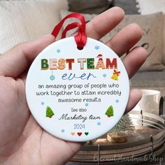 a person holding a christmas ornament with the words best team ever on it