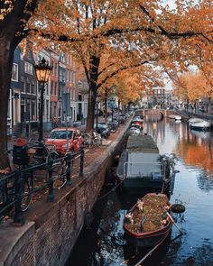 boats are parked along the side of a canal with autumn leaves on trees in the foreground