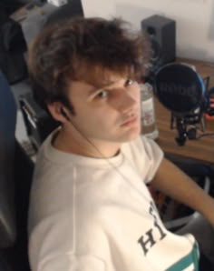 a young man sitting in front of a computer desk with headphones on his ears