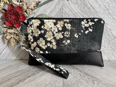 "An exterior zipper pocket can be added for an additional cost. This cute wristlet wallet is the perfect go to alternative to our everyday handbags! It will hold all your necessities including credit cards, ID and your smartphone. Super convenient for the mom on the go!! This sleek and contemporary wristlet clutch was designed using a heavy weight black fabric with a floral design. It has a black vegan leather base and a detachable strap. The well organized interior is a solid black fabric that Rectangular Black Wristlet As A Gift, Gift Clutch Wristlet With Wrist Strap, Rectangular Clutch With Wrist Strap Gift, Gift Wristlet With Wrist Strap, Black Rectangular Wristlet For Gift, Black Wristlet With Cell Phone Pocket As Gift, Gift Wristlet Clutch With Wrist Strap, Black Wristlet With Cell Phone Pocket For Gift, Rectangular Black Wristlet For Gift