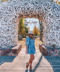 a woman standing in front of an arch made out of antelope sticks and wearing a hat