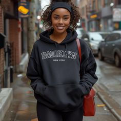 Cozy up in this Brooklyn hoodie and show off your love for the city that never sleeps. Featuring a bold red and black retro font, the word "Brooklyn" across the front makes a statement while still being a comfortable and versatile everyday wear.  Made with a soft and durable blend of materials, this hoodie will keep you warm and comfortable no matter the season. The classic design and relaxed fit make it perfect for any occasion, whether you're running errands around the city or just lounging at home.  Represent your favorite borough and add a touch of retro style to your wardrobe with this Brooklyn hoodie. It also makes a great gift for any Brooklynite or city lover in your life. So show off your pride and embrace the energy of Brooklyn with this must-have hoodie. Give a nod to the iconic Brooklyn Sweatshirt, Brooklyn Hoodie, New York Hoodie, New York Sweatshirt, New York Shirt, Sweatshirt Graphic, Retro Sweatshirts, Cotton Polyester Fabric, Black Retro