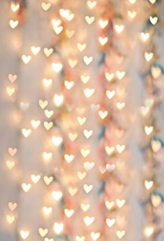 many small hearts are hanging from the ceiling in front of a white wall with lights on it